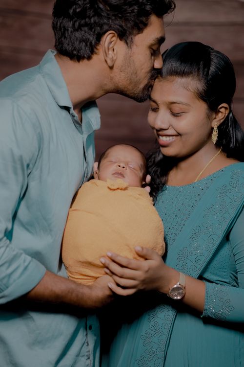Indian parents cuddling their newborn baby wrapped in a yellow blanket