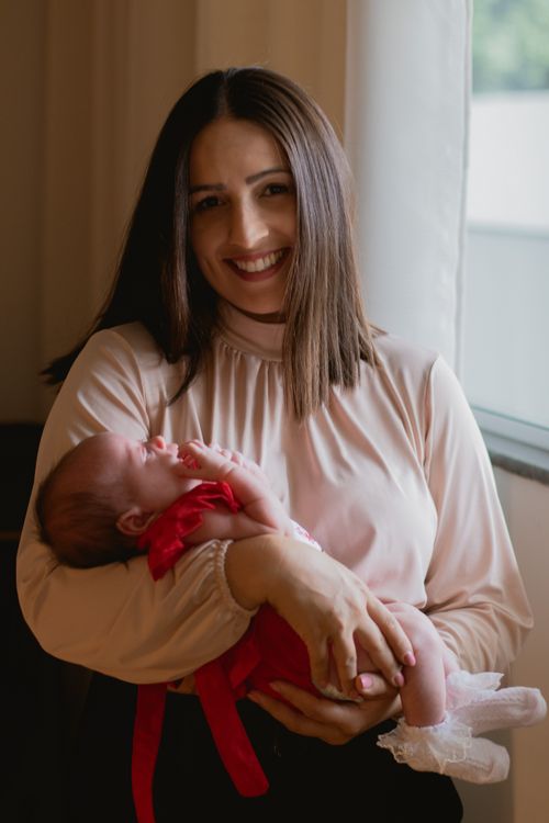 A smiling mother gently holding her newborn baby by a window